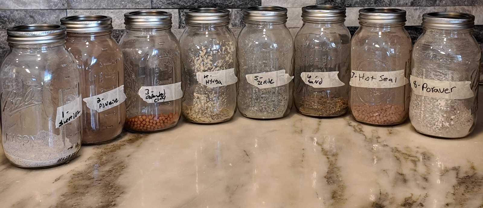 Eight numbered mason jars of substrate trial materials in a row on a kitchen counter